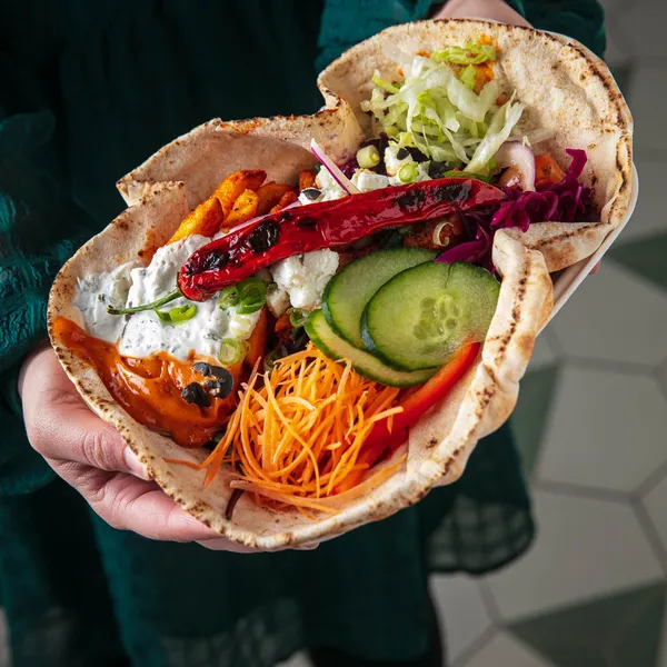 A person holding a wrap filled with colourful foods