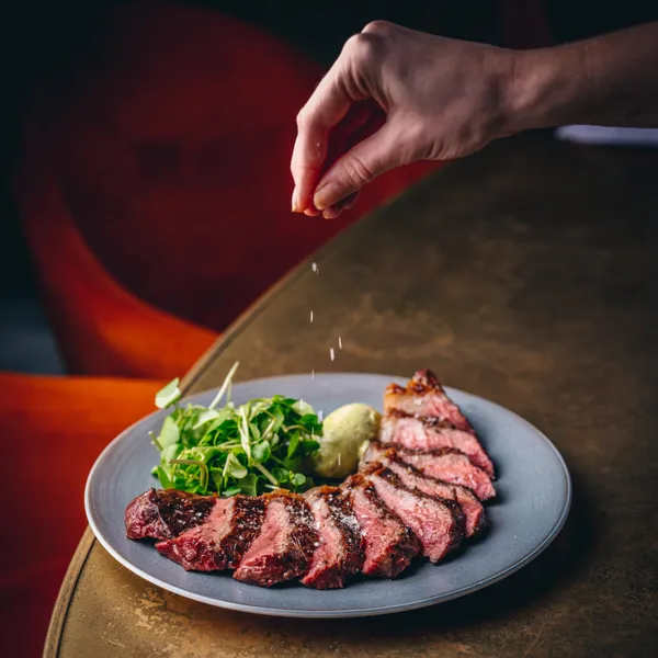Rare cooked steak on a plate, a hand is sprinkle salt over